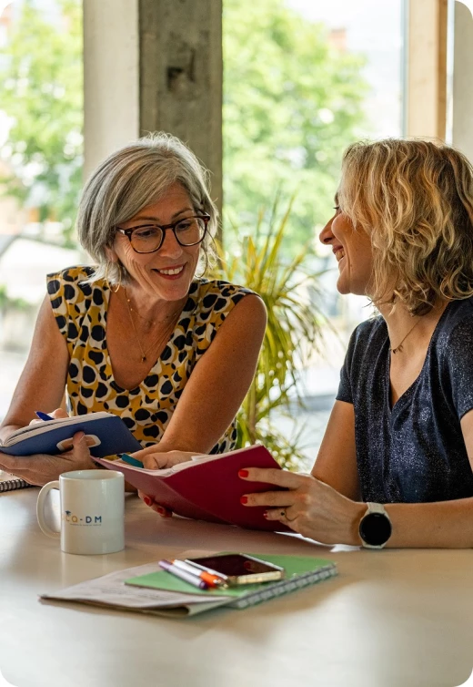 Magalie & Sonia souriantes dans une discution autour d'une table.